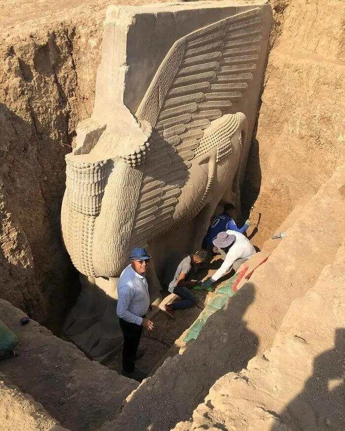 Archaeologists unearthing a massive winged bull statue, revealing cool history and ancient artifacts.