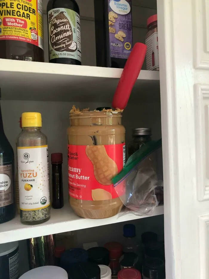 An open jar of peanut butter with a knife left stuck inside on a pantry shelf.