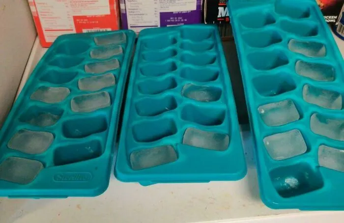 Three teal plastic ice cube trays partially filled with ice cubes, showing things partners do.