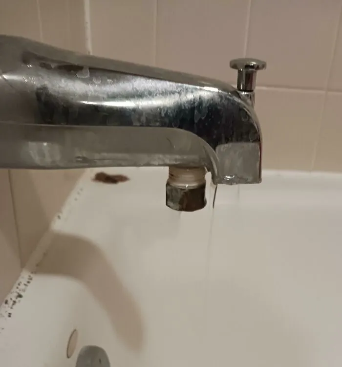 Metal bathtub faucet missing its aerator tip while water trickles out into the tub.