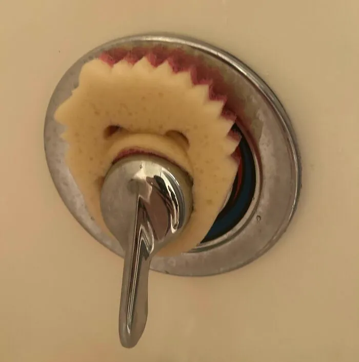 Yellow cleaning sponge wedged behind a metal shower handle in a bathroom.