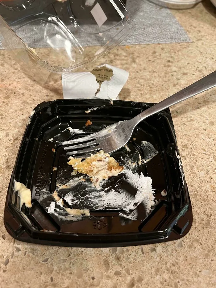 A black plastic takeout container with a fork left inside one small bite of food.