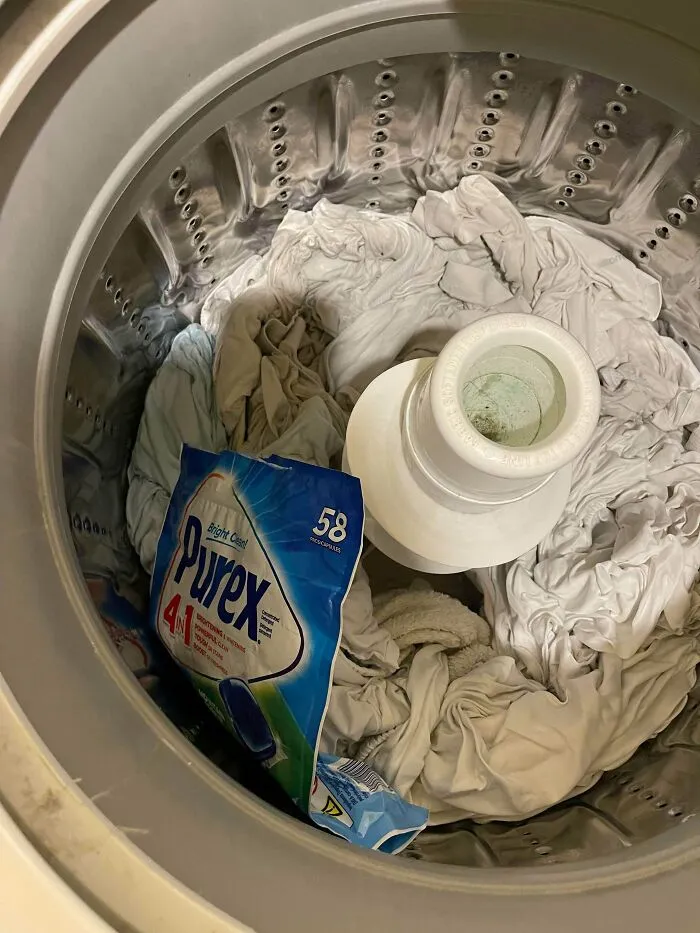 An unopened bag of laundry detergent pods tossed into a washing machine with clothes.
