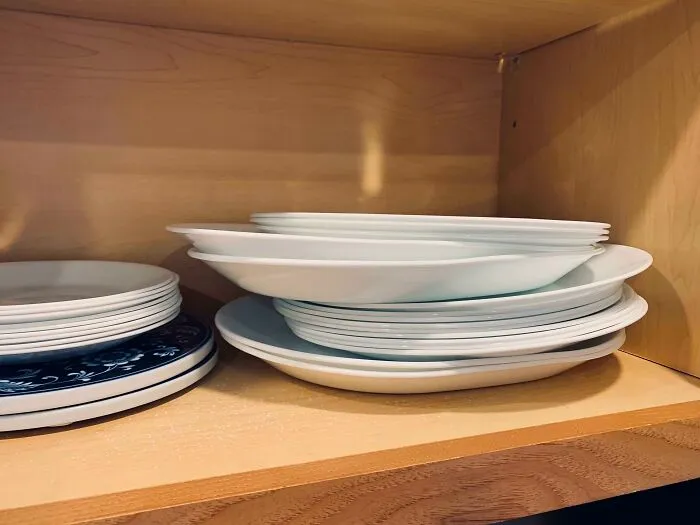 Improperly stacked white ceramic plates inside a wooden kitchen cabinet showcasing things partners do that drive people insane