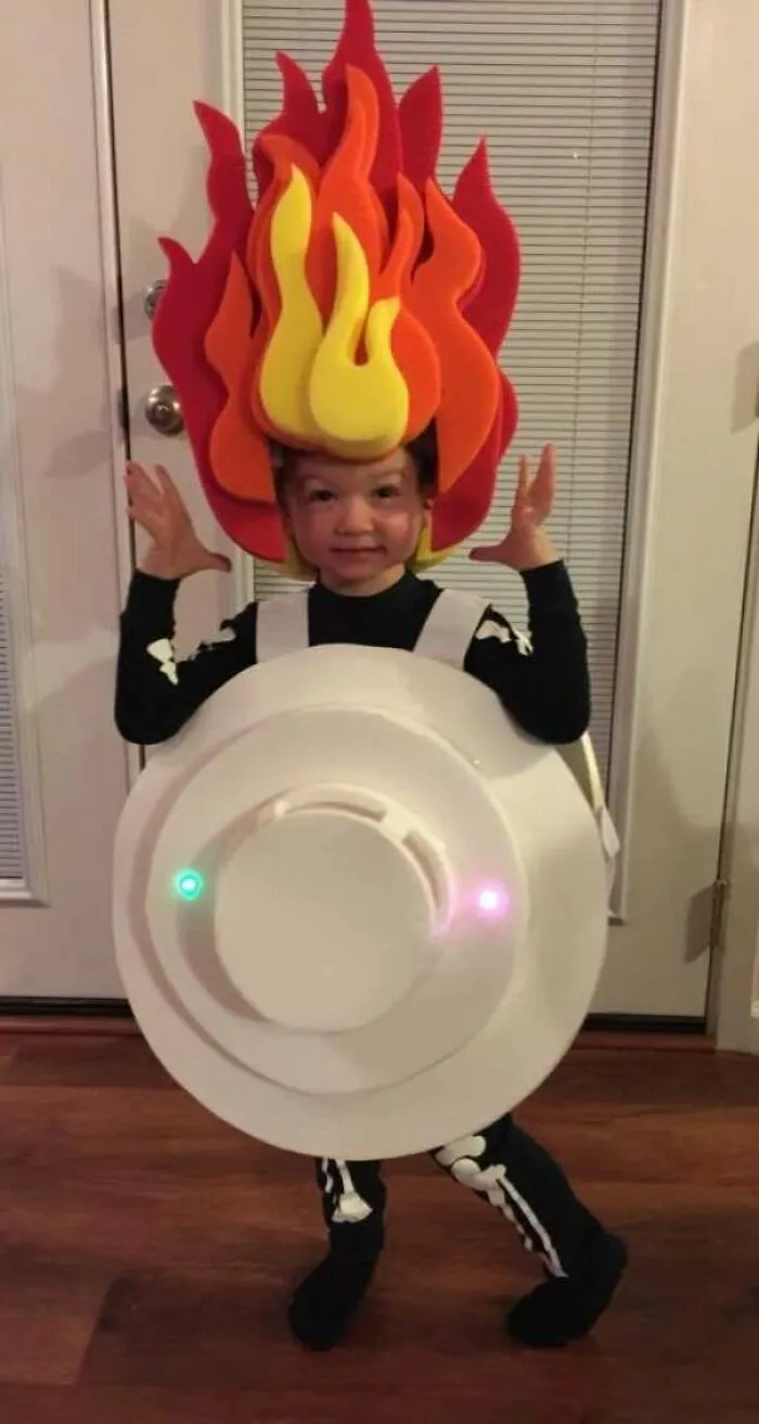 Child wearing Halloween costumes designed like a smoke detector with felt fire flame headpiece.