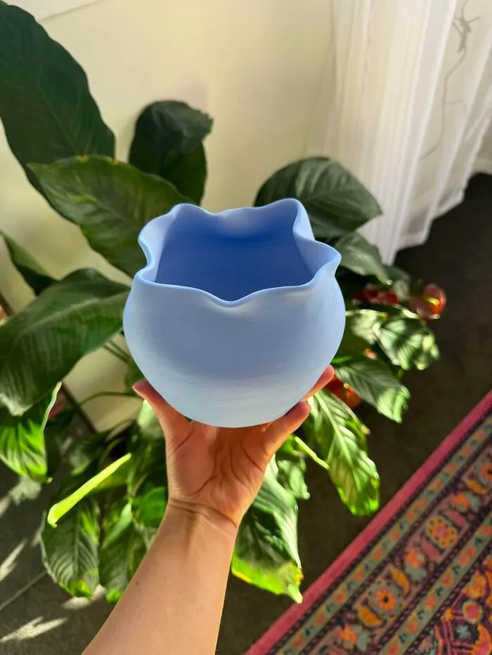 Hand holding a light blue wavy ceramic vase, an example of handmade pottery creations