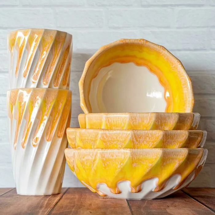 Set of yellow and white textured ceramic bowls and cups displaying handmade pottery creations