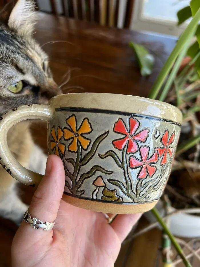 Handcrafted ceramic mug with floral engravings and cat showing beautiful pottery creations