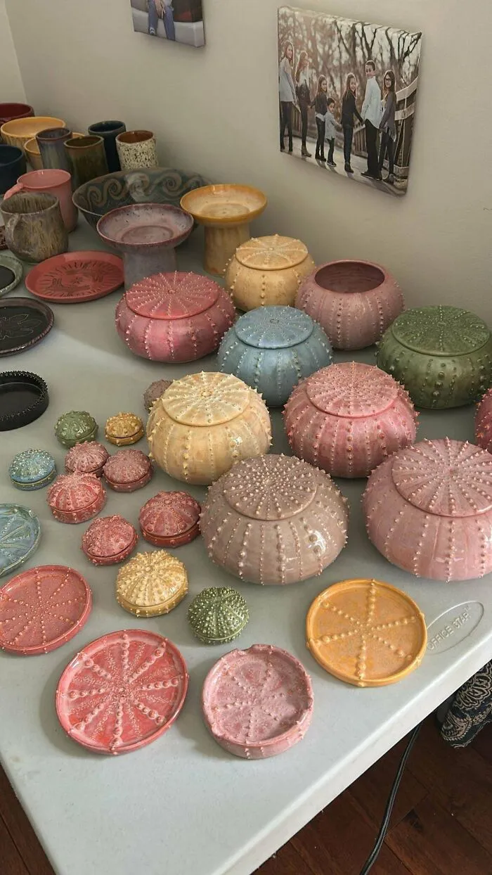 A table full of colorful sea urchin-inspired pottery creations with textured lids and saucers.