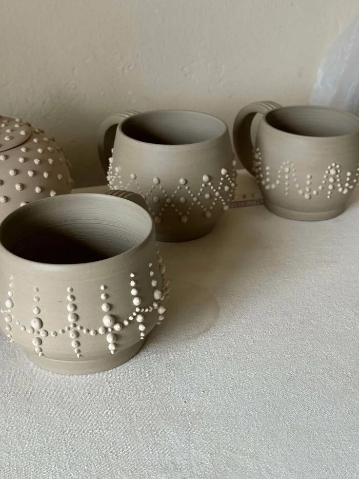 Handcrafted beige clay mugs featuring raised dot details as pottery creations.