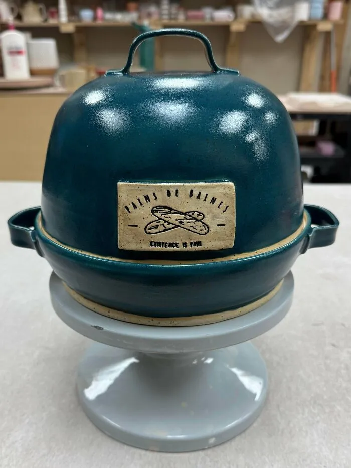 Teal ceramic bread baker showing pottery creations on a stand.