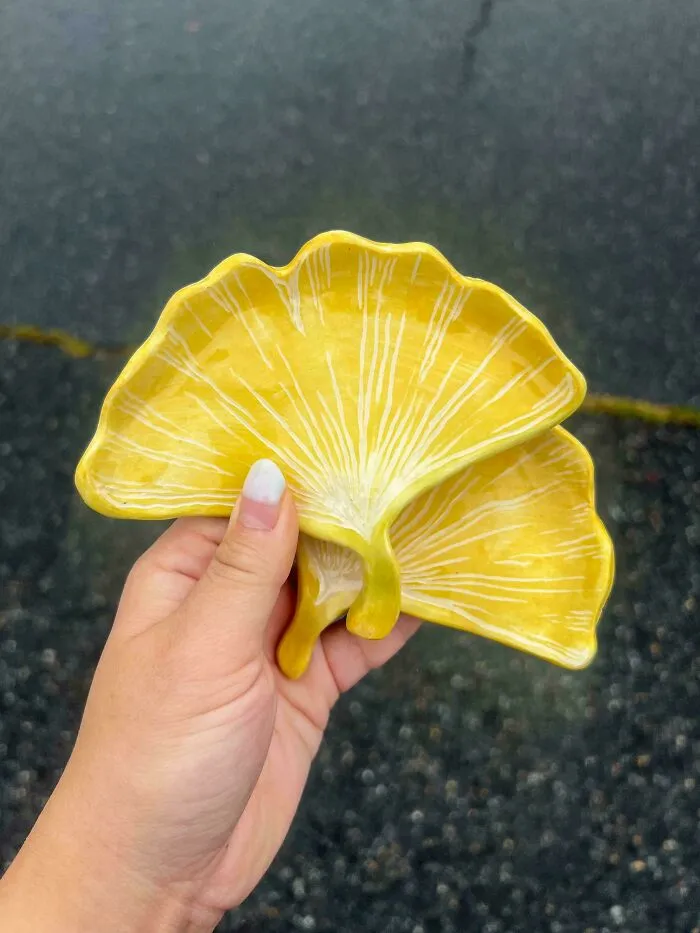 Hand holding yellow ginkgo leaf pottery creations with intricate white leaf veins.