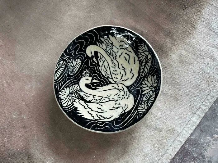 A black and white ceramic plate featuring swans and water lilies as part of pottery creations
