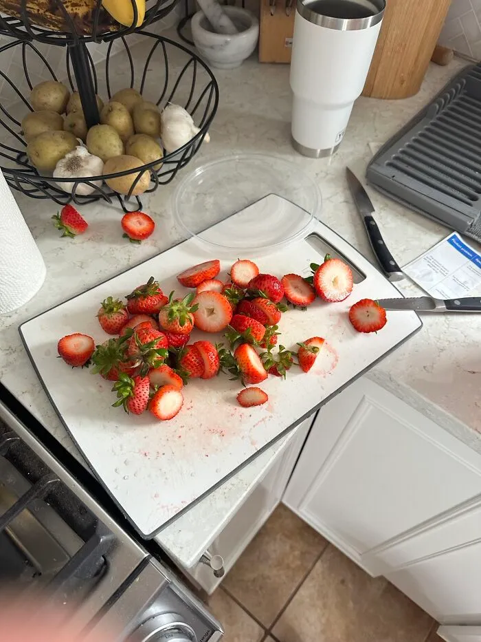 Strawberries with tops sliced off on a cutting board by a partner