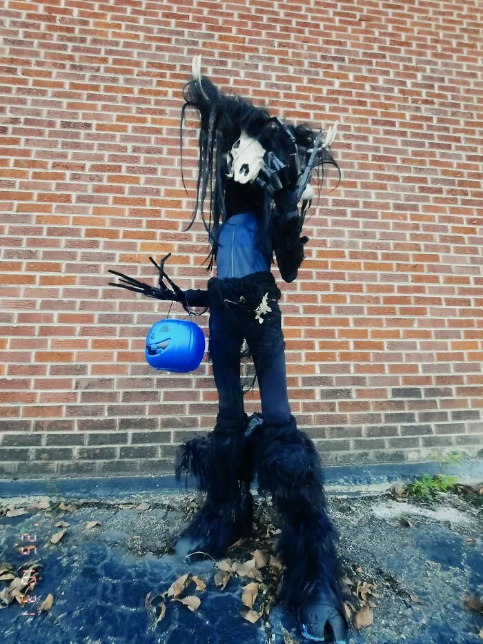 A person wearing a dark, tall mythical creature Halloween costume carrying a blue bucket