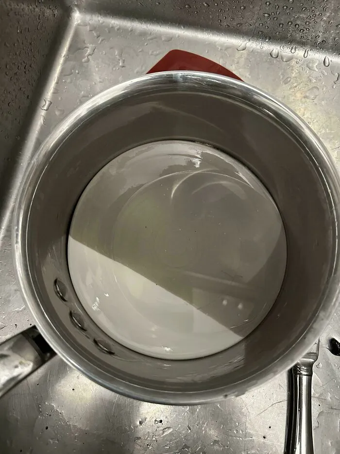 White ceramic plate stuck perfectly inside the bottom of a metal cooking pot in a kitchen sink.