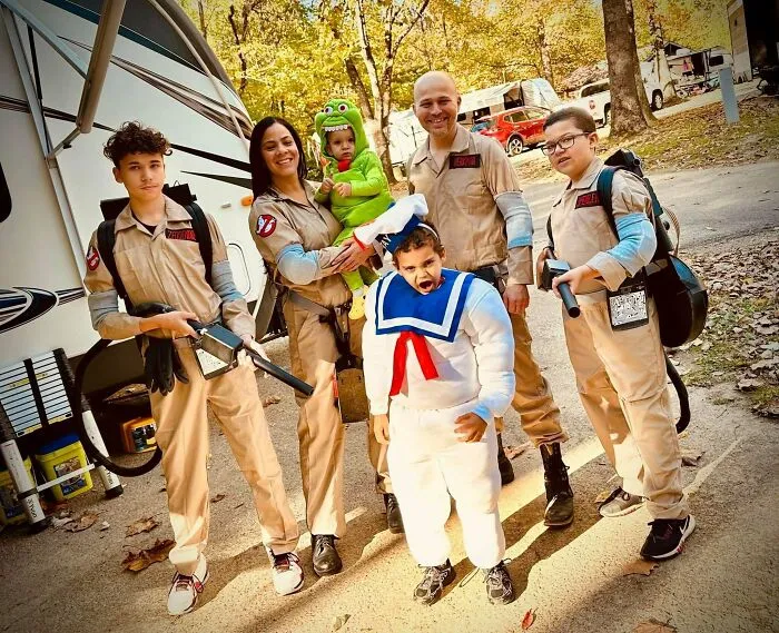 A family dressed as Ghostbusters showing off creative Halloween costumes together outdoors.