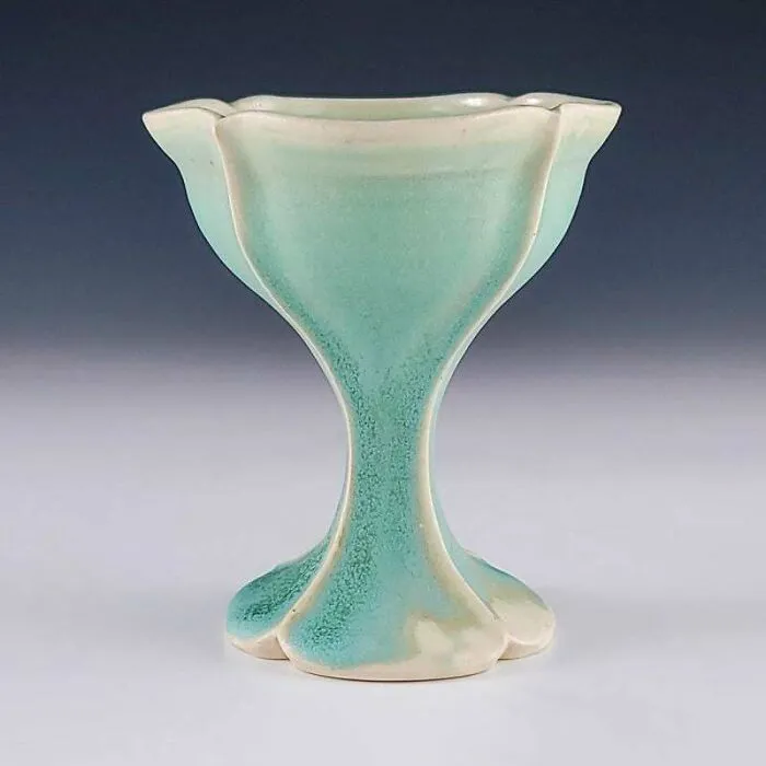 An elegant light teal chalice-shaped vase displaying handmade pottery creations.