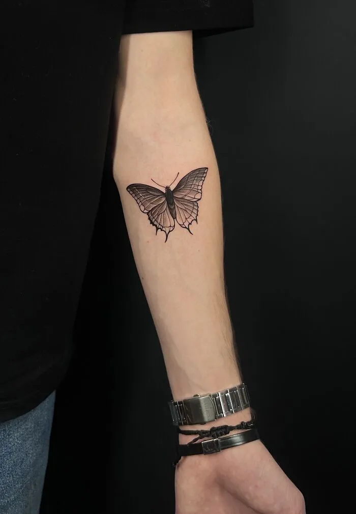 Black and gray butterfly tattoo on inner forearm