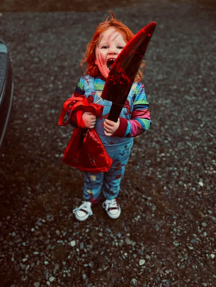 A child wearing a creepy horror movie Chucky style Halloween costume with a large fake knife.