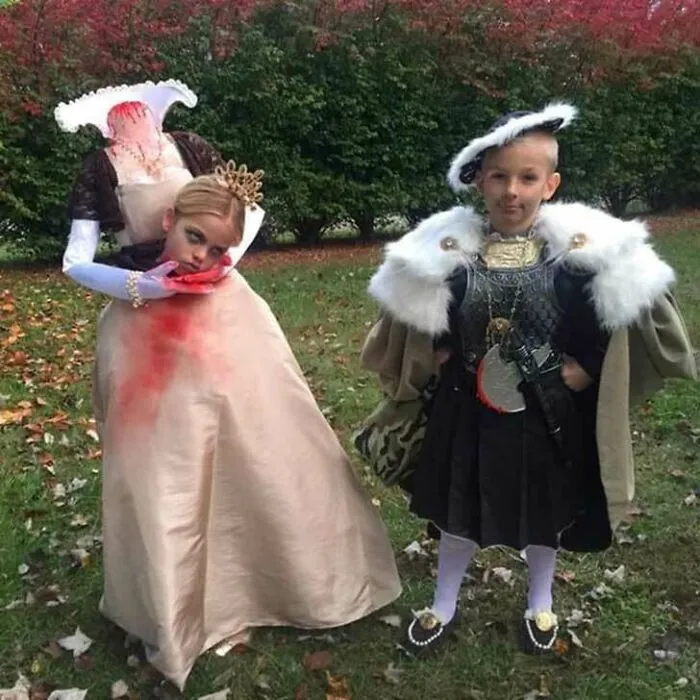 Two children wearing elaborate headless queen and king kids Halloween costumes outdoors.