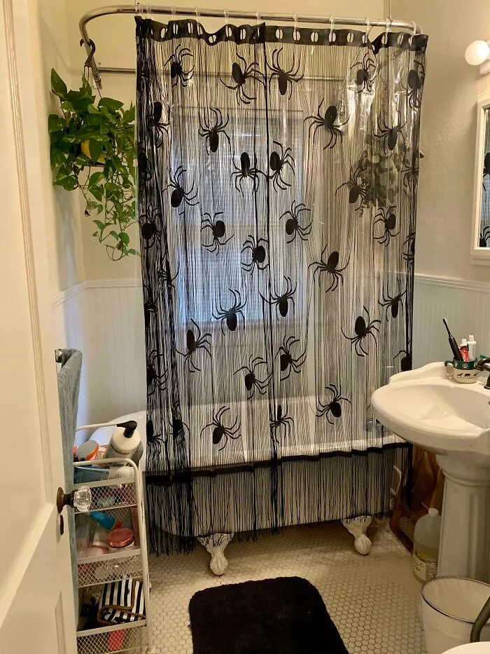 Black spiderweb shower curtain hanging in a decorated bathroom with a clawfoot tub for Halloween.