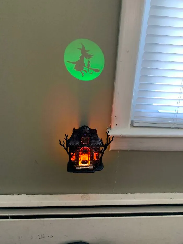 A glowing Halloween night light displaying a witch silhouette on the wall near a window sill