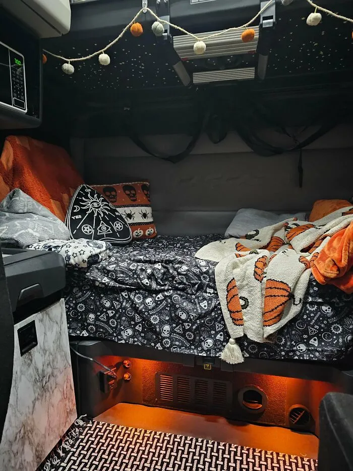 A semi-truck sleeper cab cozy bed area styled with spooky Halloween bedding, pillows, and string lights