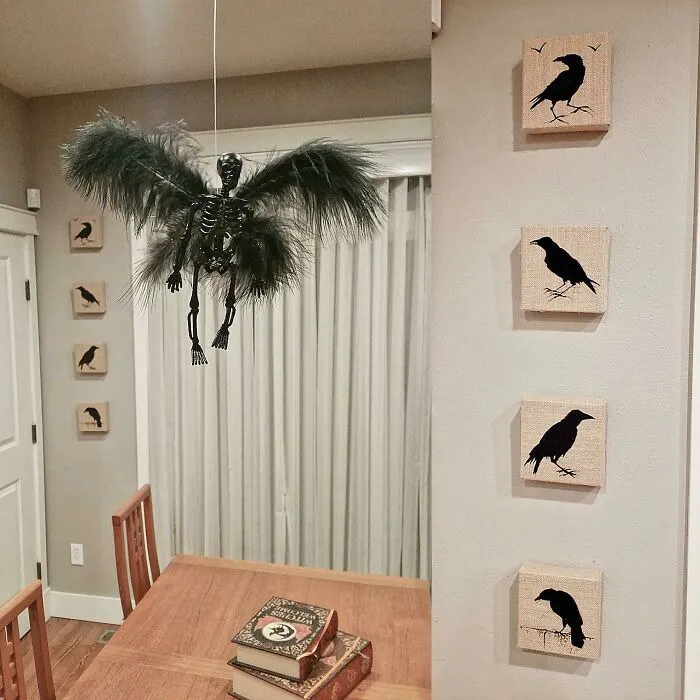 A flying winged skeleton hanging over a table surrounded by crow wall art for a Halloween home decoration setup
