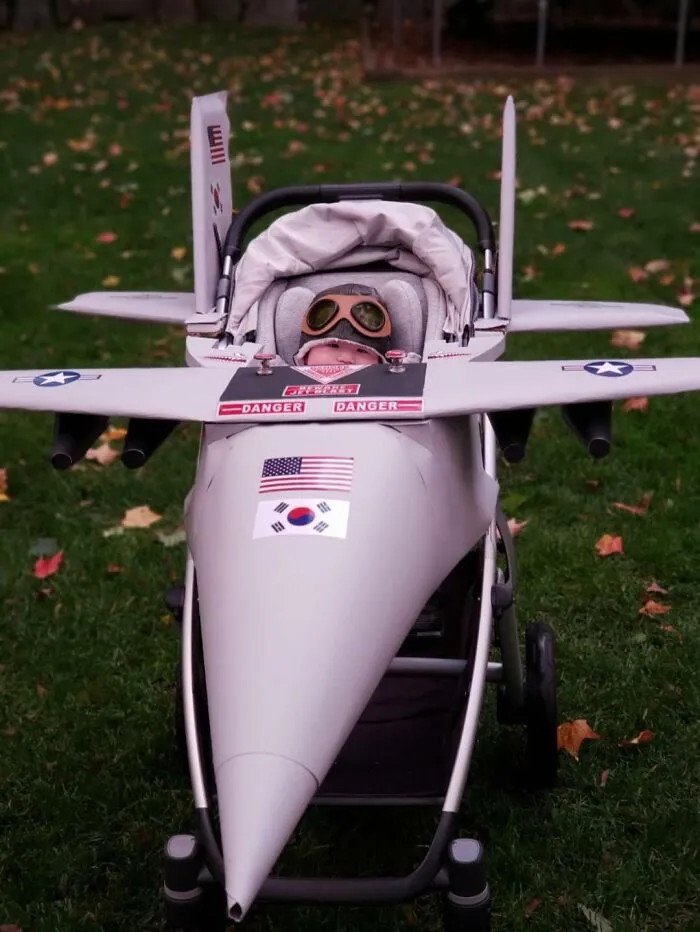 A baby sitting in a fighter jet stroller costume for creative kids Halloween costumes.
