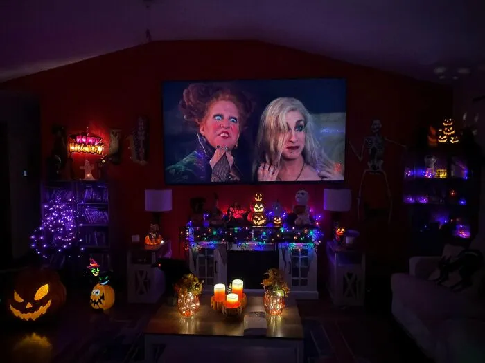 Cozy living room setup for Halloween with a TV playing Hocus Pocus, lit pumpkins, and spooky lights.