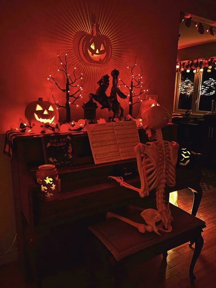 Halloween decor featuring a skeleton seated at an upright piano surrounded by lit jack-o-lanterns.