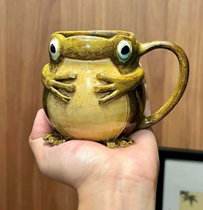 A hand holding a ceramic frog mug, showcasing unique pottery creations.