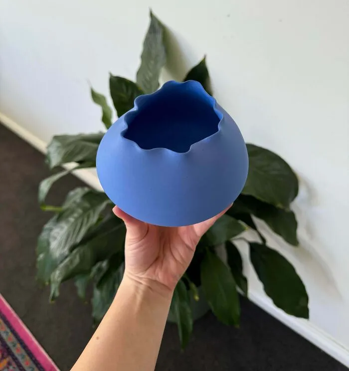 Hand holding a matte blue vase, displaying unique pottery creations.