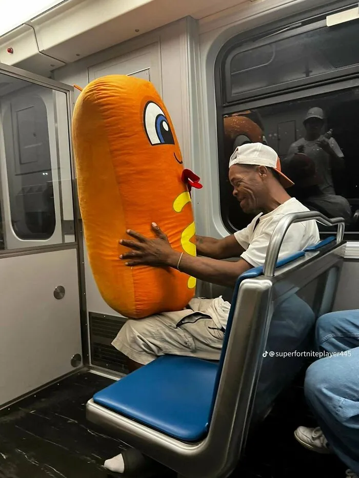 Man holding a giant plush hotdog on a train, sharing wholesome moments with travelers