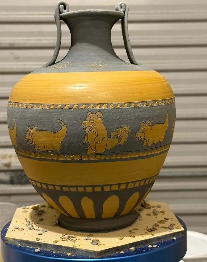 A grey and yellow Greek amphora-style vase with carved cartoon characters, showcasing custom pottery creations.
