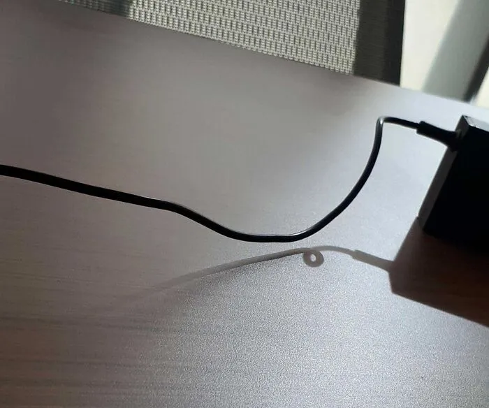 Shadow of a charging cable forming a loop on a table mimicking a digital glitch effect