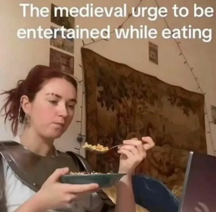 Relatable memes image of a person eating while watching a screen in medieval armor