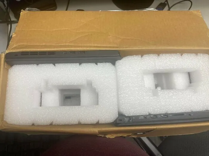 Two laptops packed tight inside a cardboard box with foam inserts, showcasing excessive packaging fails.