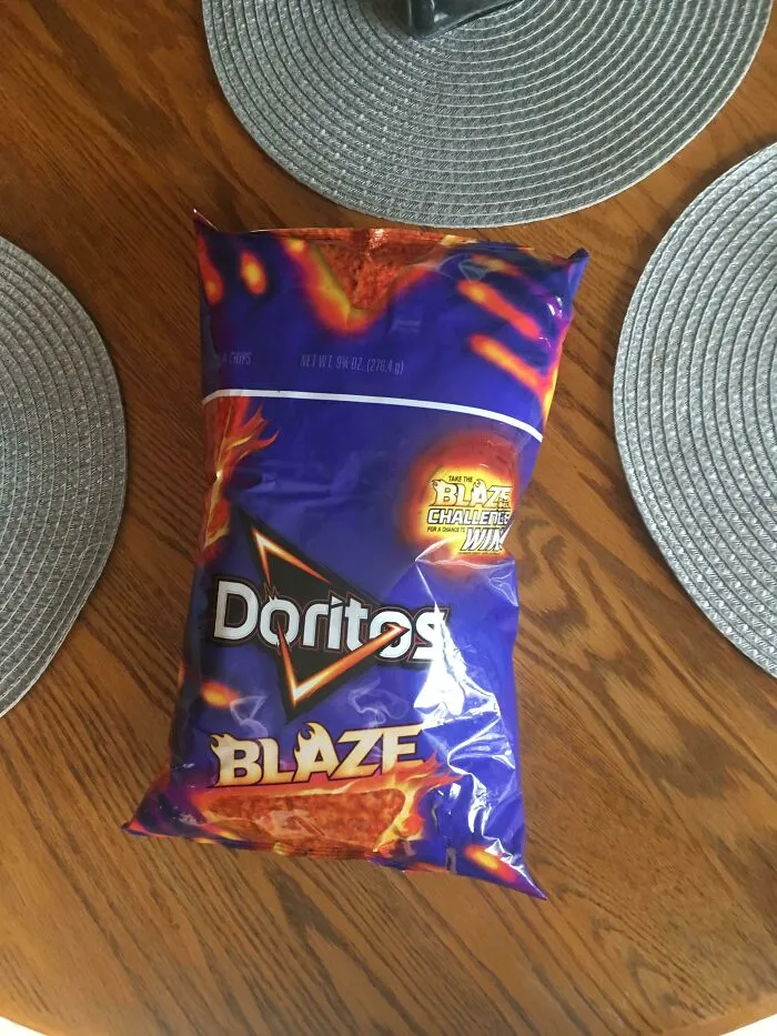 An upside down bag of Doritos Blaze chips demonstrating a funny packaging fail on a wooden table.