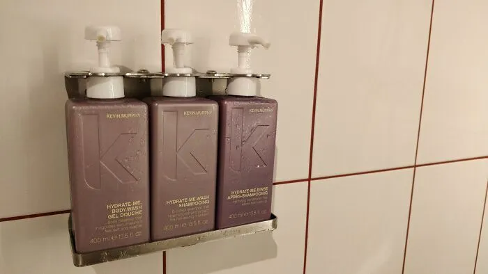 Three shower product bottles mounted on a wall bracket with logos displaying a KKK initial packaging fail.
