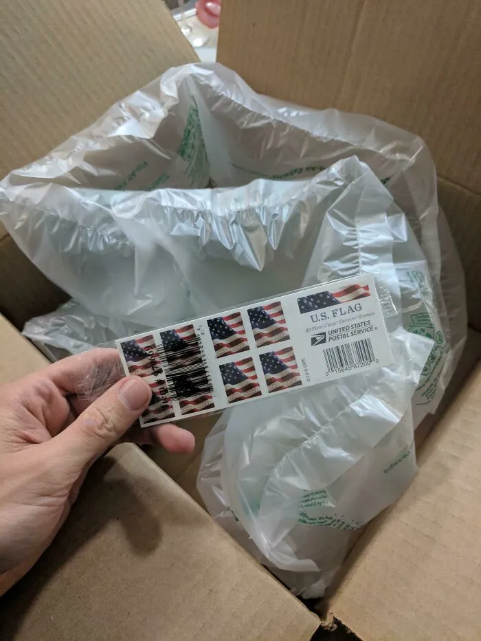 Small sheet of US Flag stamps inside a large box filled with air pillows depicting bad packaging fails