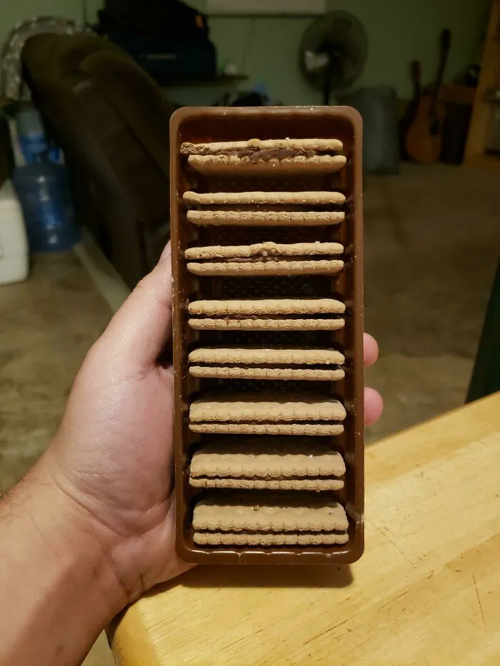 A hand holding a brown plastic cookie tray with empty slots showing a bad packaging fail
