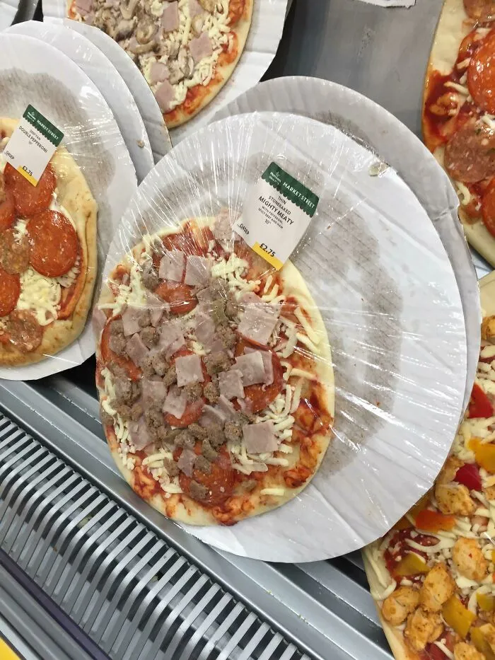Uncooked pizza wrapped in plastic on a tray, highlighting a packaging fail.
