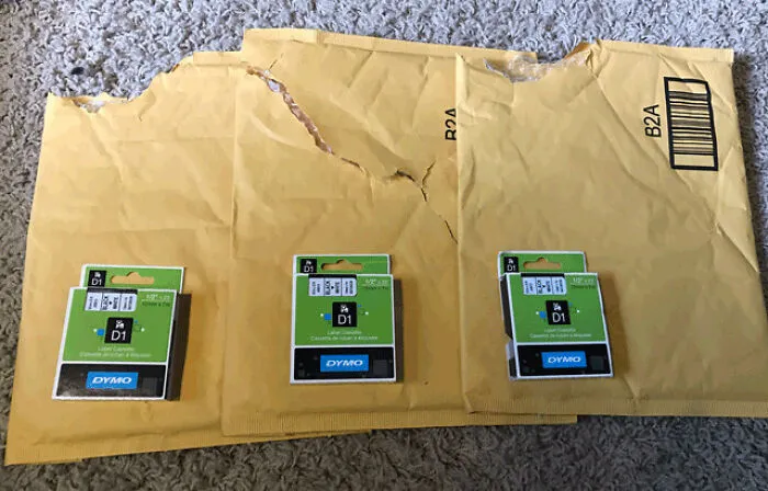 Three small label cassettes in huge padded envelopes, showing wasteful packaging fails.
