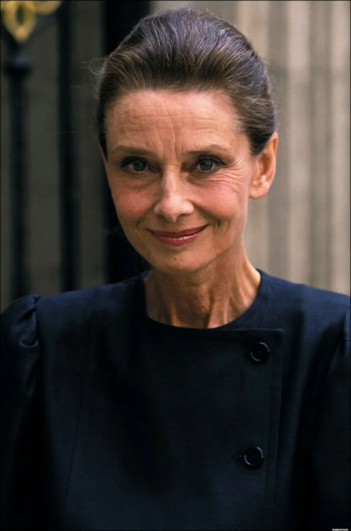 Audrey Hepburn smiling gently in a dark coat, captured in photos for the last time during her later years