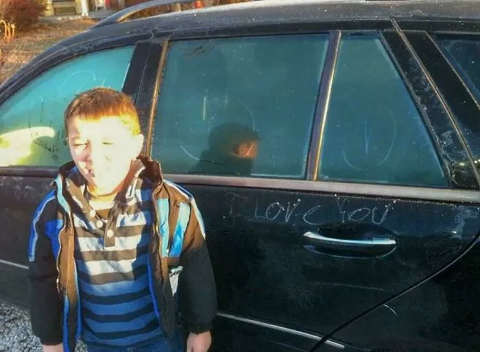 Young boy captured in photos for the last time standing by a dark car with writing on the window.