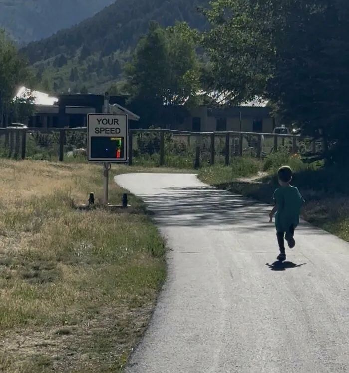 A young child running along a path towards a speed radar sign, showing wholesome pics of dads parenting.