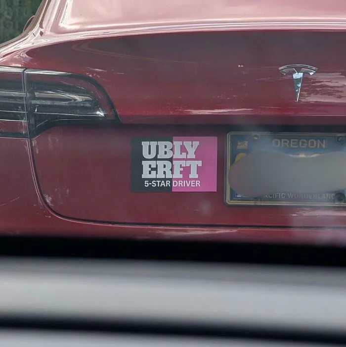 A bumper sticker with poorly aligned text on a red Tesla car, showcasing terribly designed signs.
