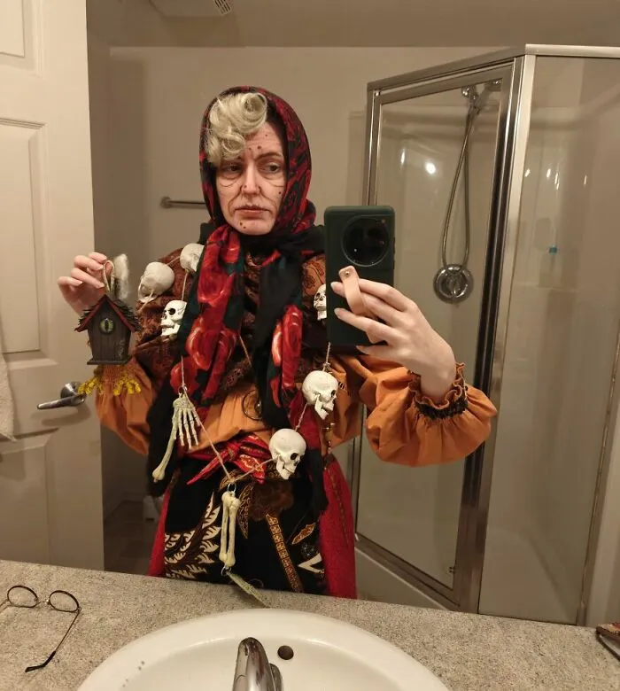 Woman taking a bathroom selfie dressed as a witch with skull decor for a creative Halloween costume idea.